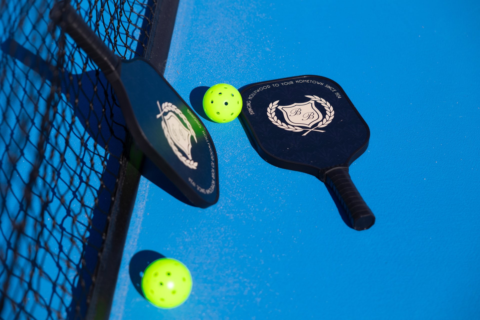 2 pickleball bats and balls on a playing court with a net